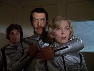 A large Italian man holds Barbara at gunpoint in Main Mission, while his girlfriend looks on.