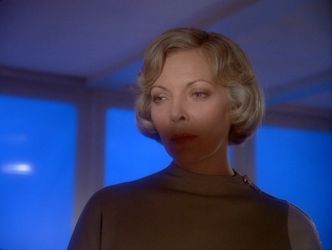 Barbara is in sickbay, standing in front of one of Alpha's glowing blue walls. Her face is half in shadow, and she is glaring disapprovingly at someone off camera.