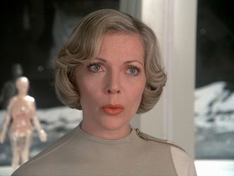 Barbara stands in front of a window in sick bay, her eyes wide and her lips pursed. She looks concerned.