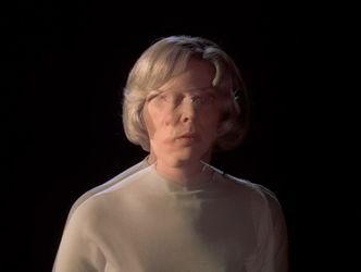 Barbara stands in a blank void, her face blurring and overlapping eerily.